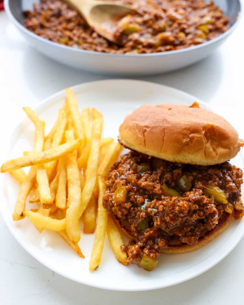 An overhead view of a turkey sloppy Joe sandwich with fries on the side and a pan full of sloppy Joe mixture in the background.