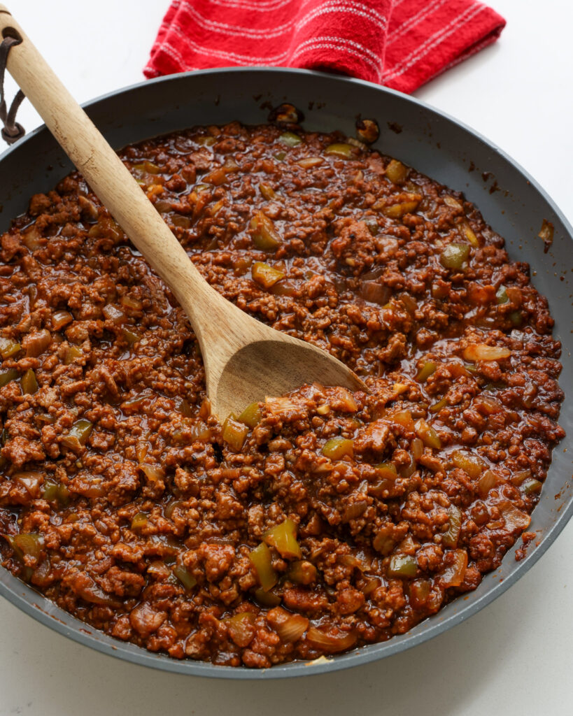 A pan and a wooden spoon full of sloppy Joe mixture.