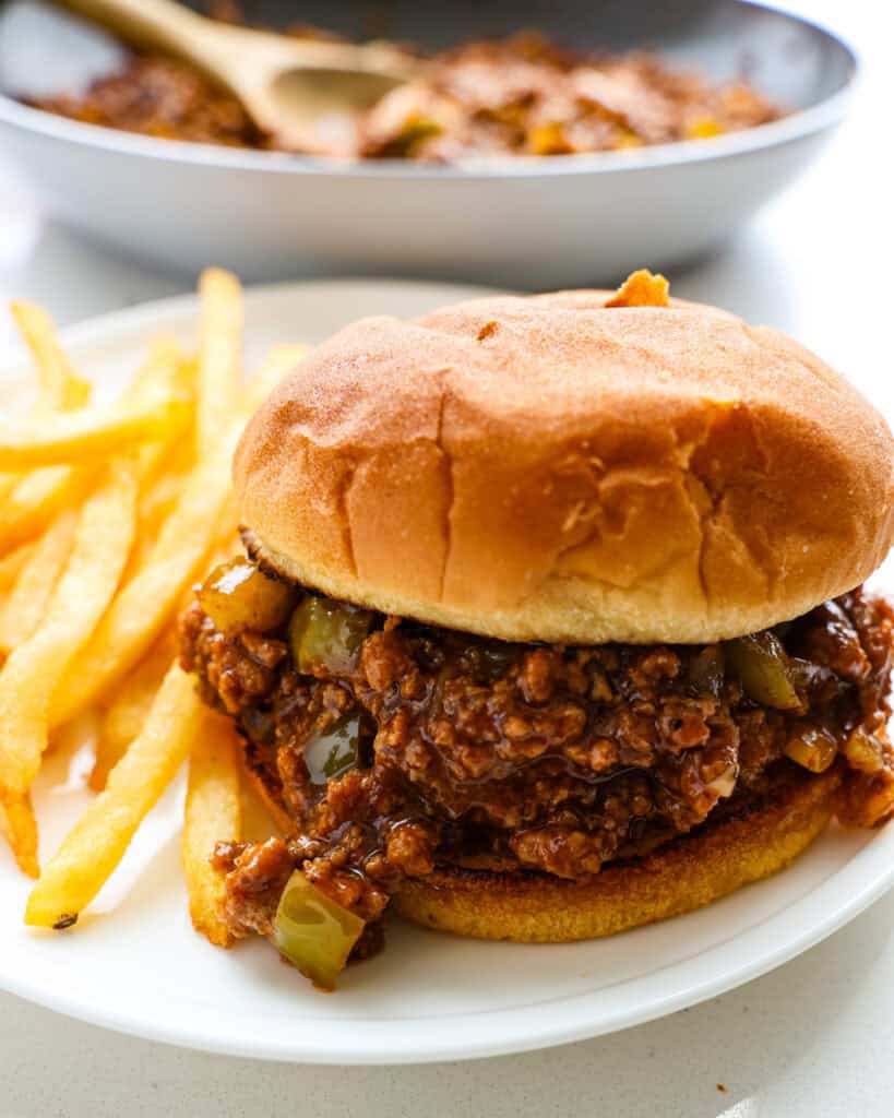 A close up view of turkey sloppy Joe mixture on a toasted bun with French fries on the side.