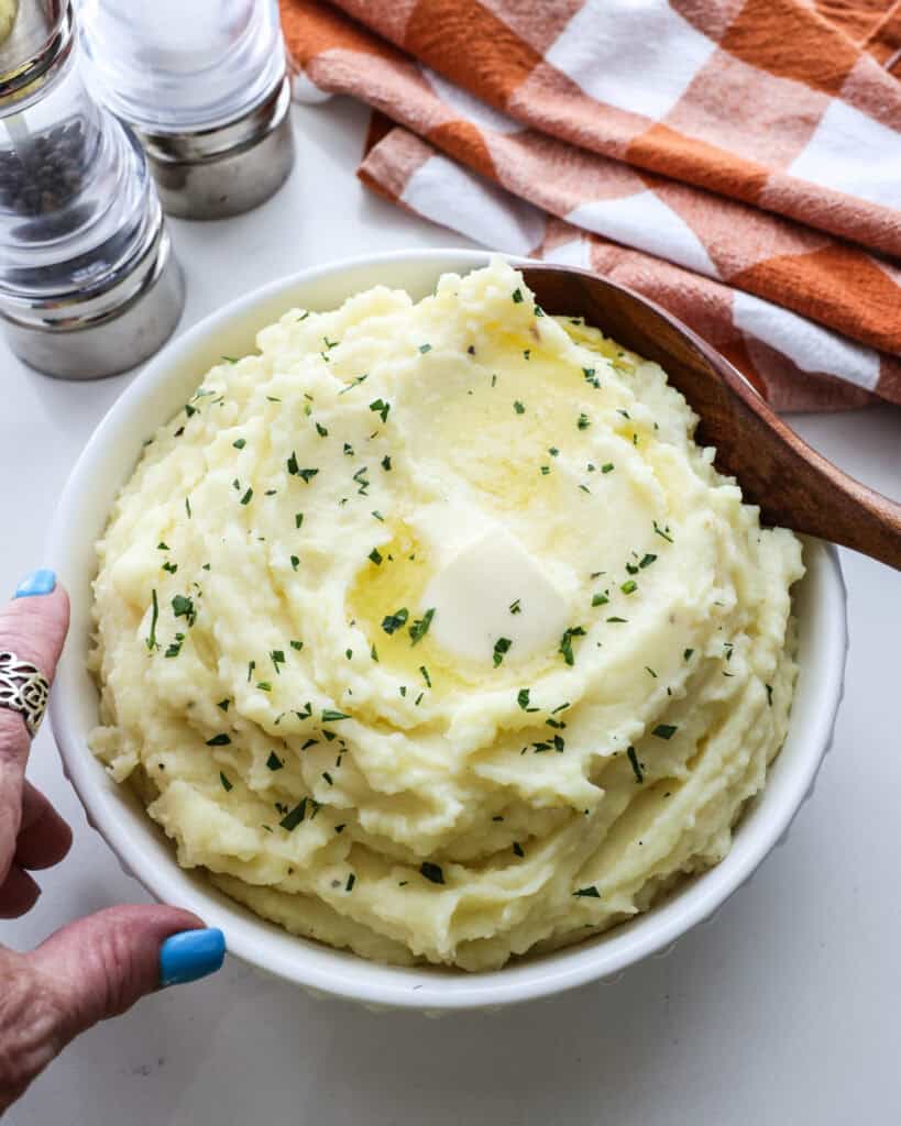 A serving bowl full of Yukon Gold Mashed poatoes with a kitchen towel and salt and pepper sharker in the background.