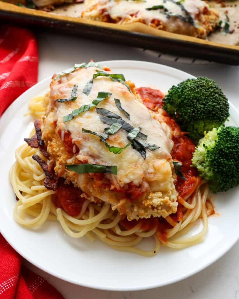 Baked Parmesan chicken on a bed of spaghetti with steamed broccoli on the side. 