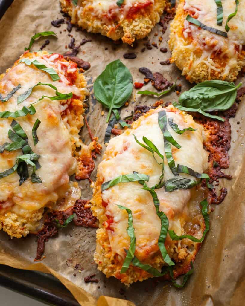 Four baked chicken parmesan breasts on a parchment covered baking sheet. 