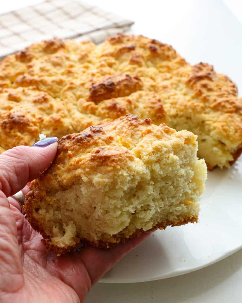 A held up cathead biscuit over a a plate full of cathead biscuits.