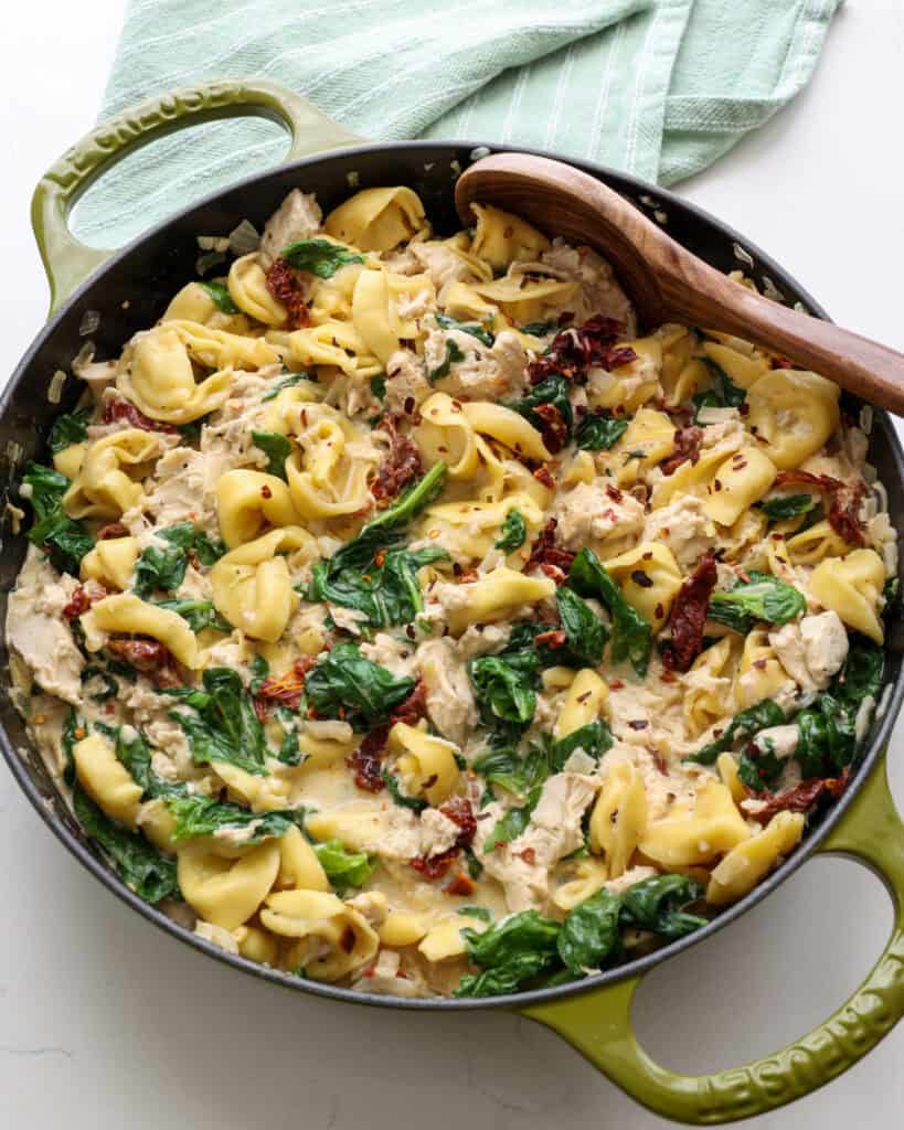 A skillet full cheese tortellini, spinach, chicken, and sun-dried toimatoes.