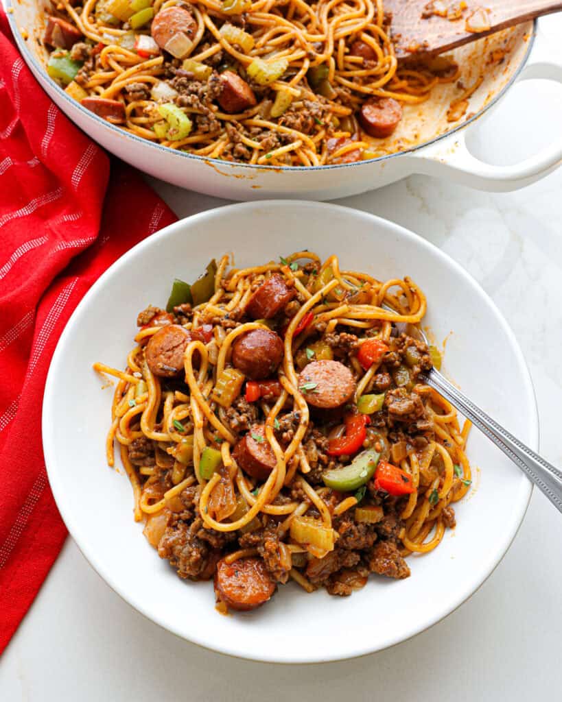 A single serving bowl full of dirty spaghetti with a Dutch oven full of it in the background. 