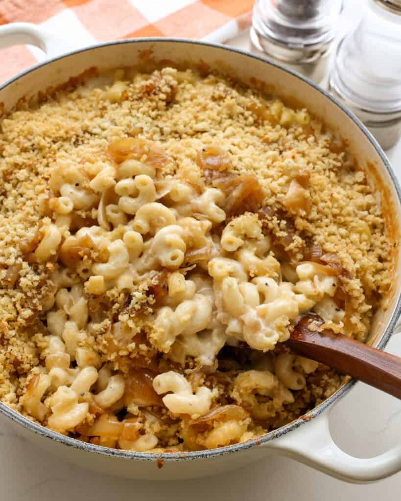 A white Dutch oven and a wooden spoom full of French onion mac and cheese. 