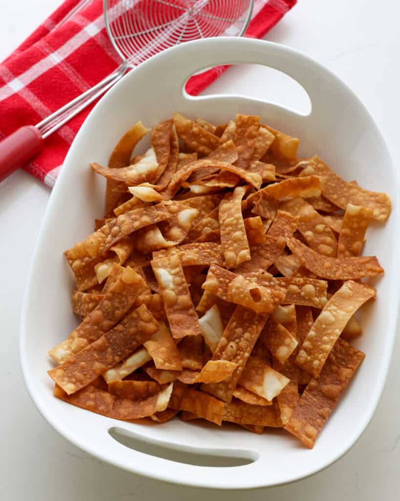 A big bowl of fried wonton strips with a spider strainer in the background.