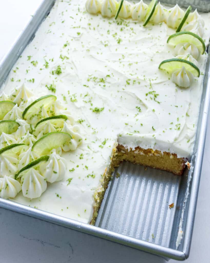 A 9x13 inch metal pan with a key lime cake in it with a slice removed. 