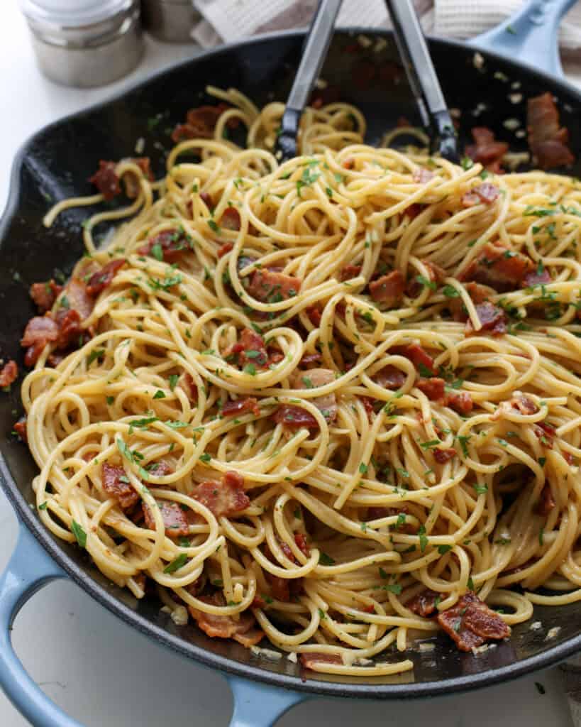 A skillet full of spaghetti carbonara with tongs in the skillet.