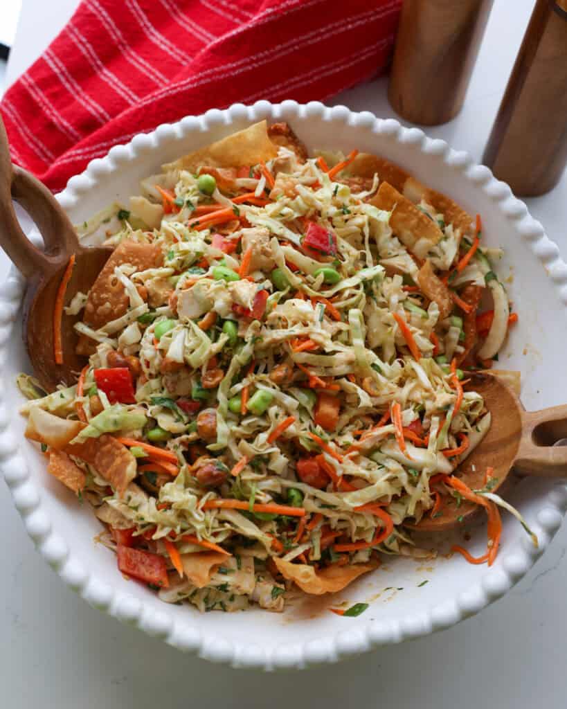 A large white bowl ful of Thai chicken salad with wooden salad tossers in the bowl.