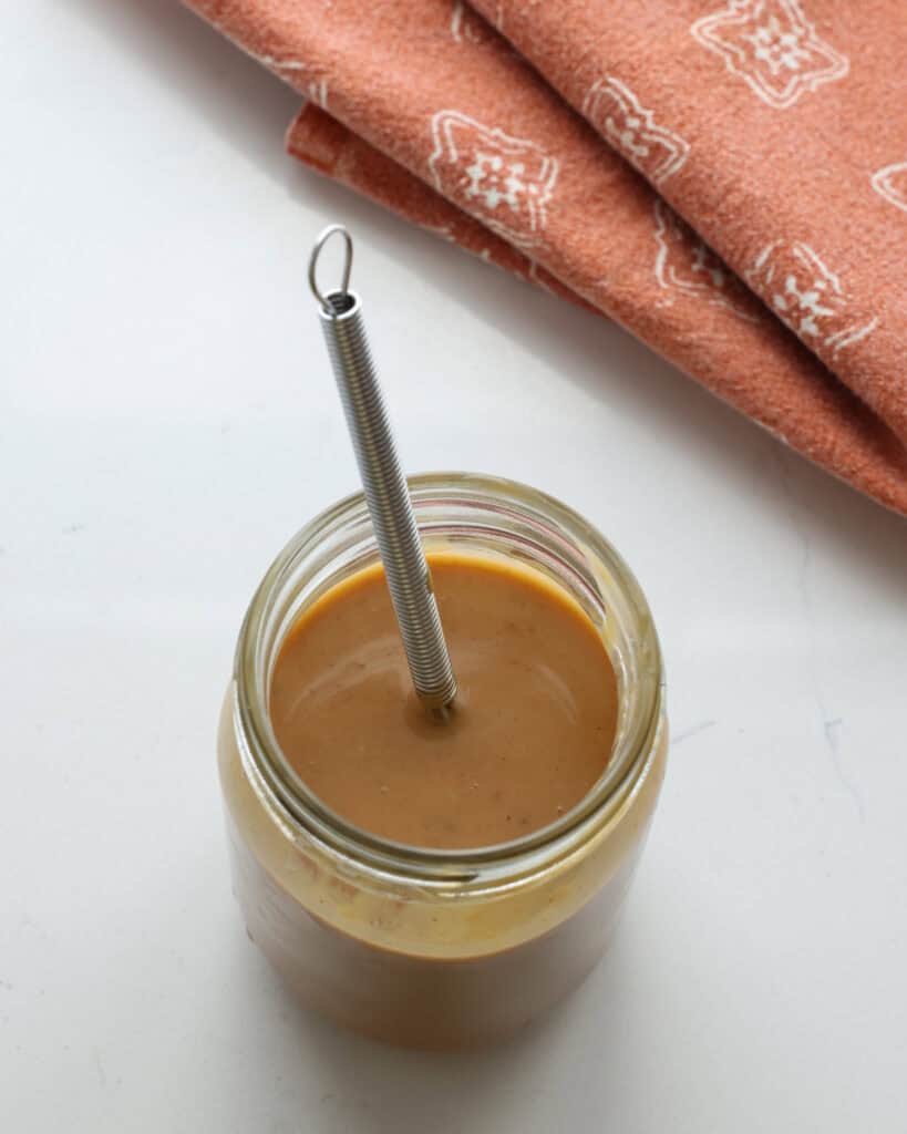 Thai peanut dressing in a mason jar with a whisk.