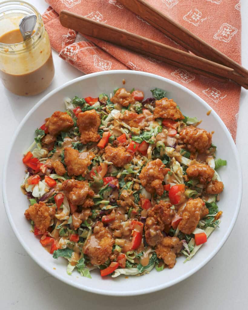 An Asian salad with red bell peppers, cabbage, and green onions drizzed with Thai peanut dressing.