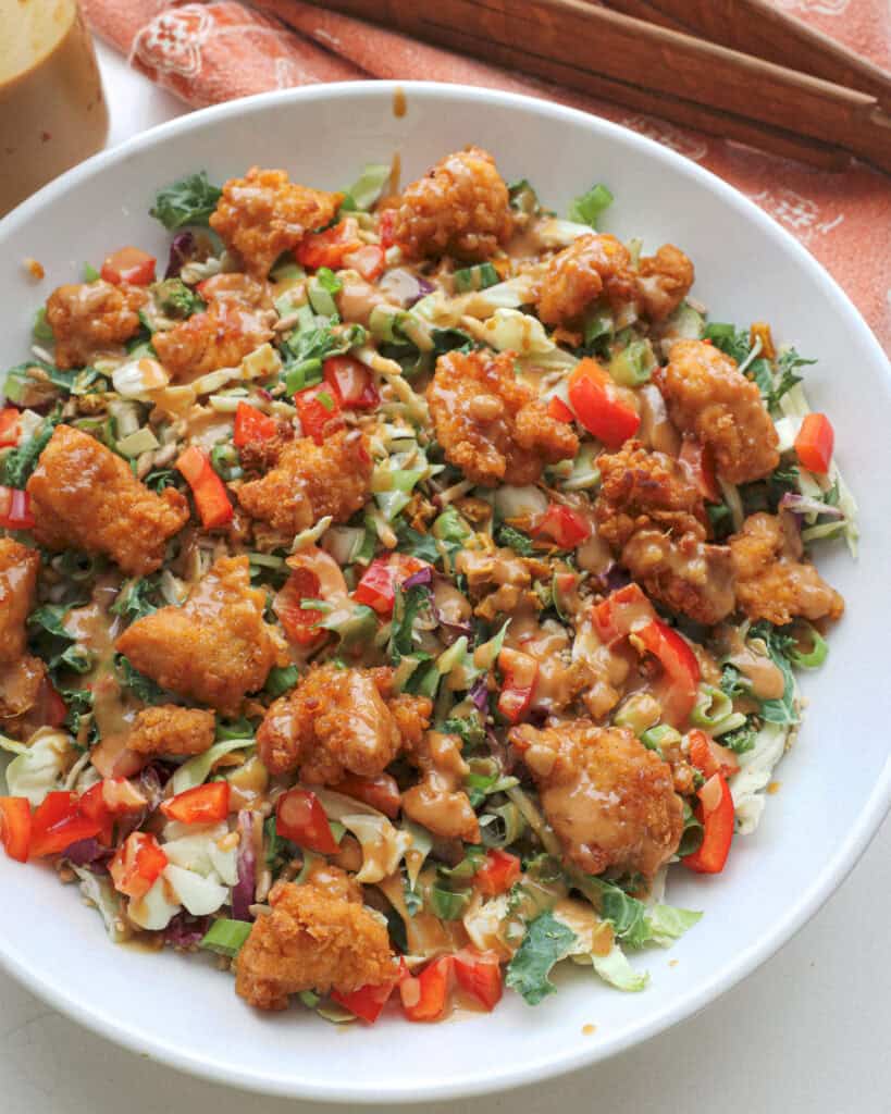 A close up view of an Asian salad drizzled with That peanut dressing in a large white serving bowl.