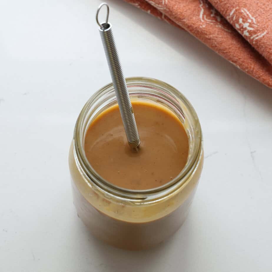 Thai peanut dressing with a whisk in a mason jar.