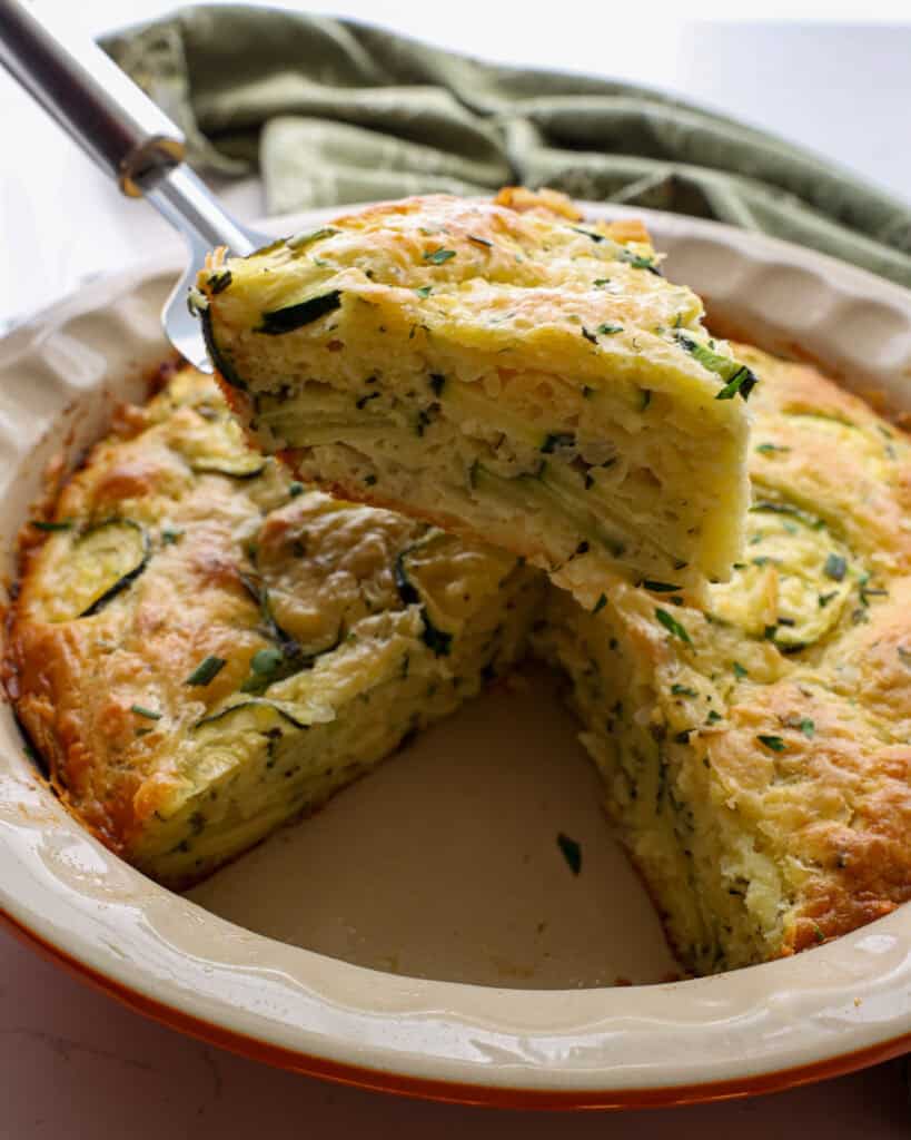 A slice of zucchini pie over a pie pan filled with zucchini pie. 