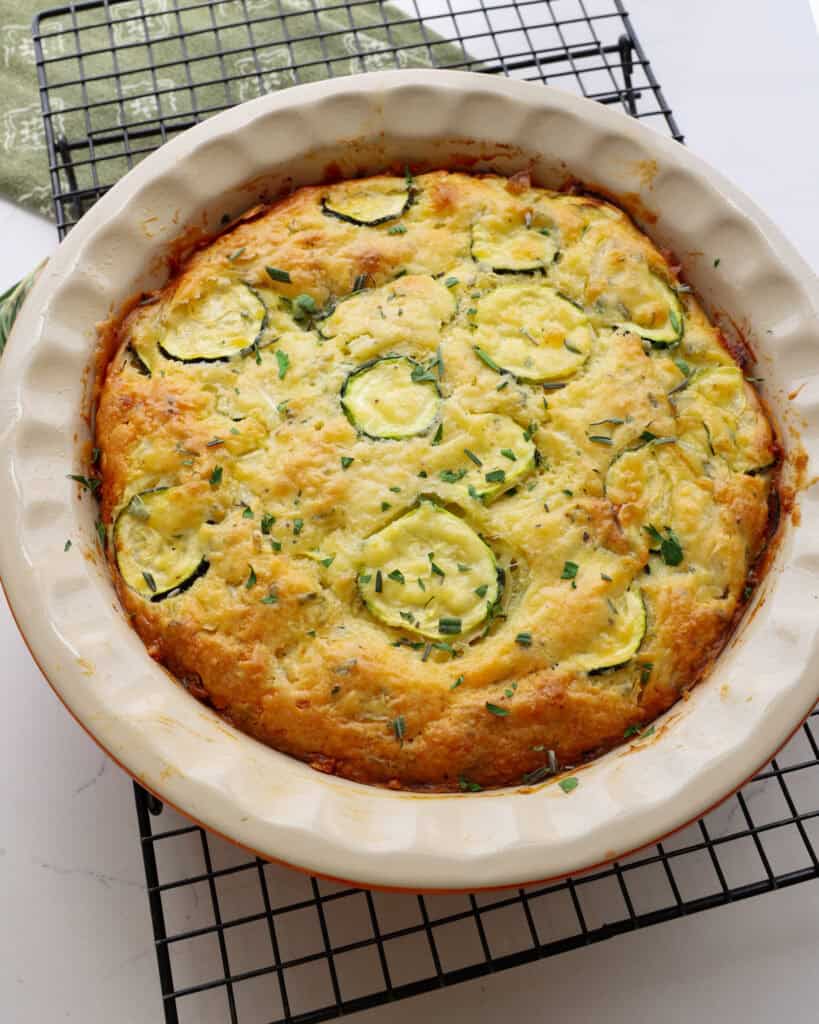 A zucchini pie in a pie pan cooling on a wire rack. 