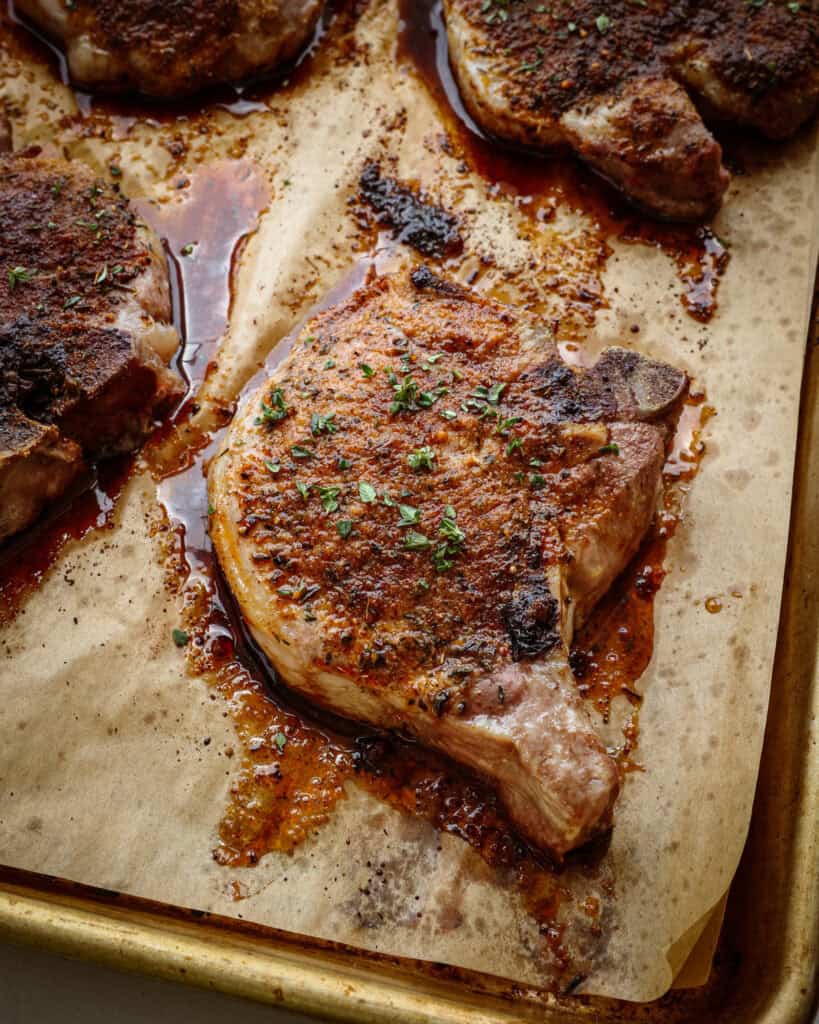 An oven baked pork chop sprinkled with chopped fresh thyme on a baking sheet covered with parchment paper.