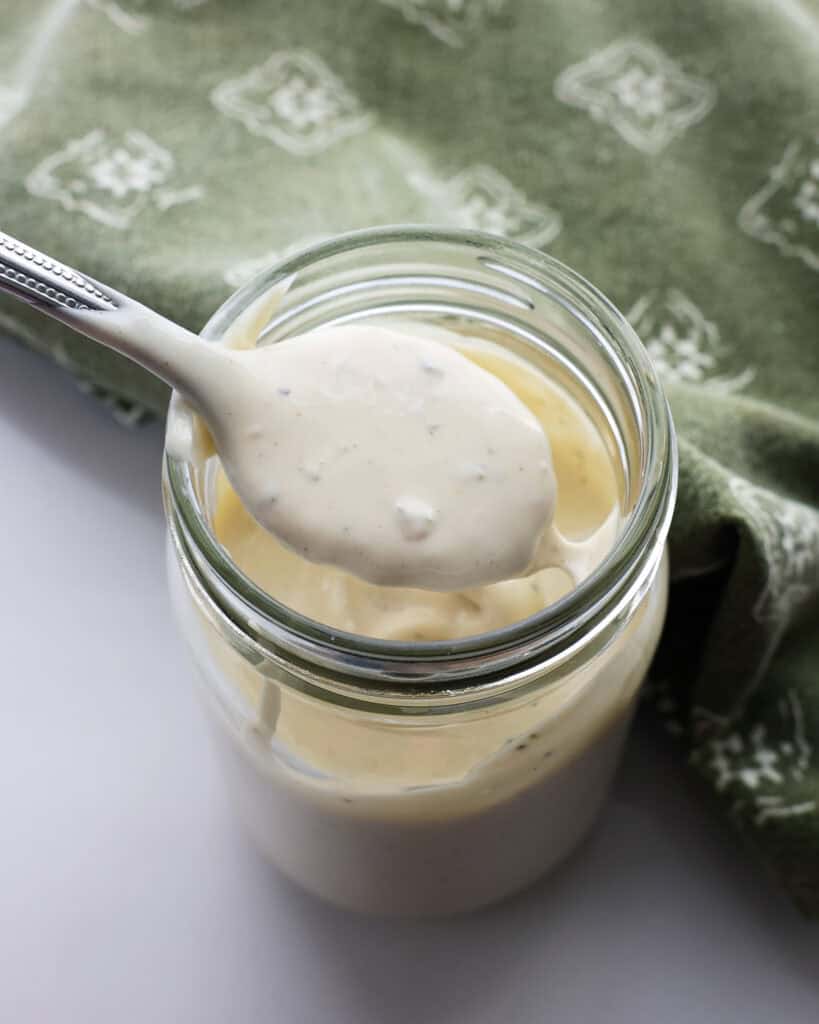 A spoon full of Caesar dressing over a mason jar full of Caesar dressing.