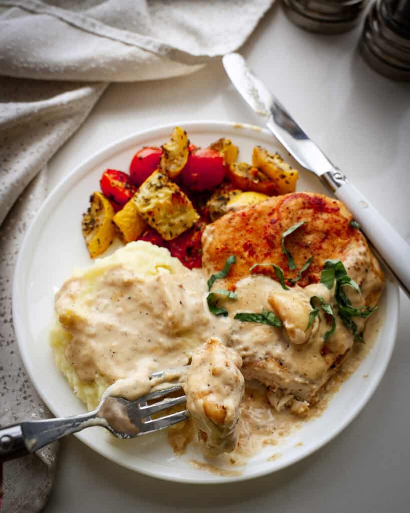 Creamy garlic chicken, mashed potatoes, and yellow squahs with tomatoes on a single white serving plate.