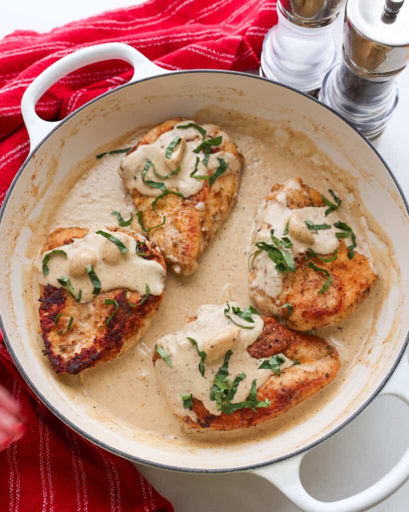 An overhead view of four lightly breaded and browned chicken breast with creamy garlic sauce.