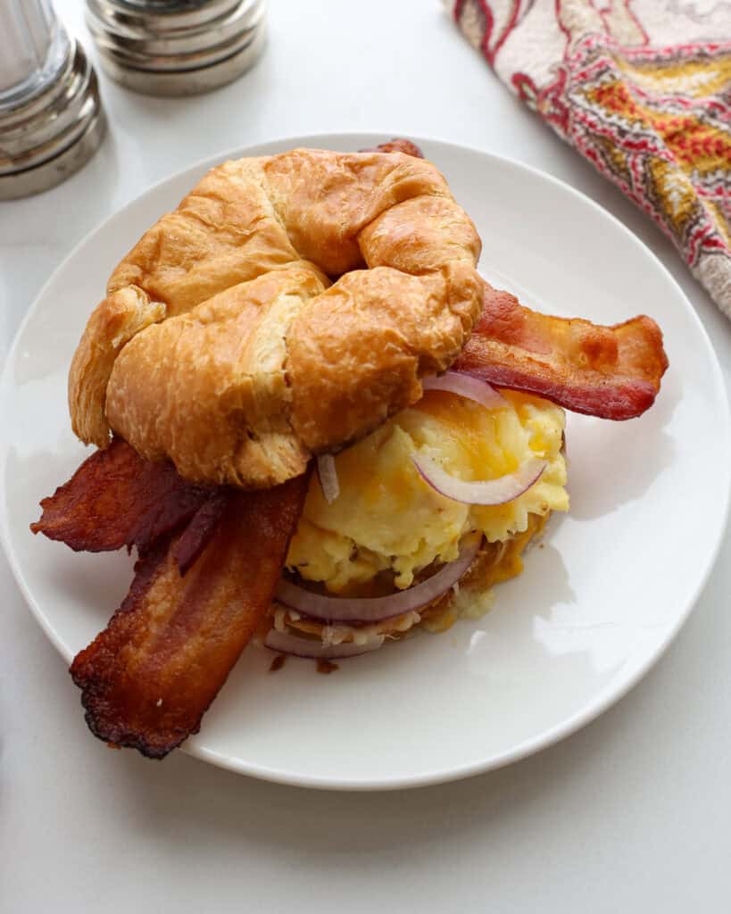 A close up view of a croissant breakfast sandwich with scrambled eggs, cheese, and bacon.