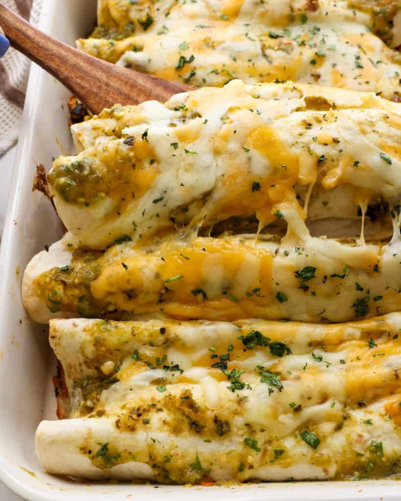 A baking dish and a wooden spatula full of enchilada verdes.