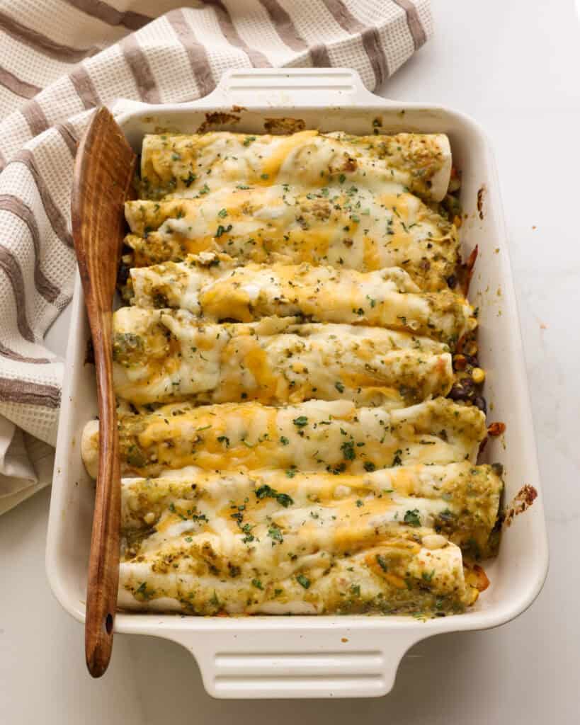 An overhead view of a casserole dish full of enchilada verdes with a kitchen towel in the background.