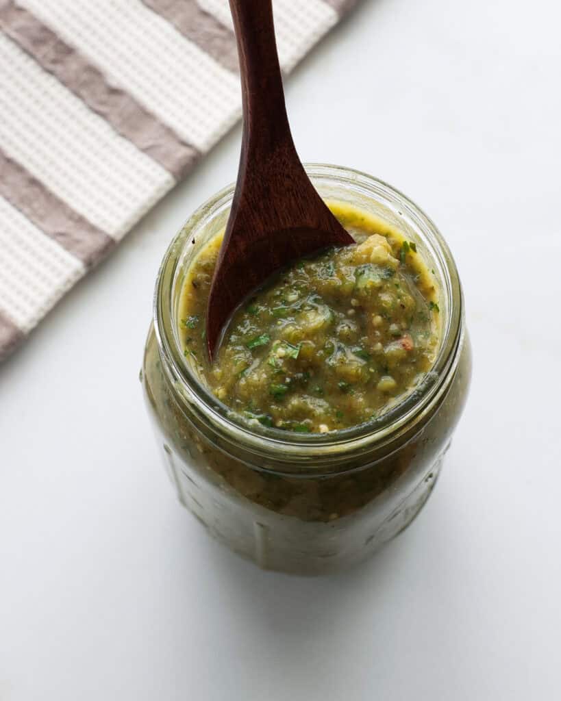 A mason jar and a wooden spoon with enchilada sauce.