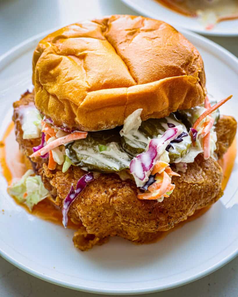 A close up view of a hot honey chicken sandwich on a sigle serving white plate.