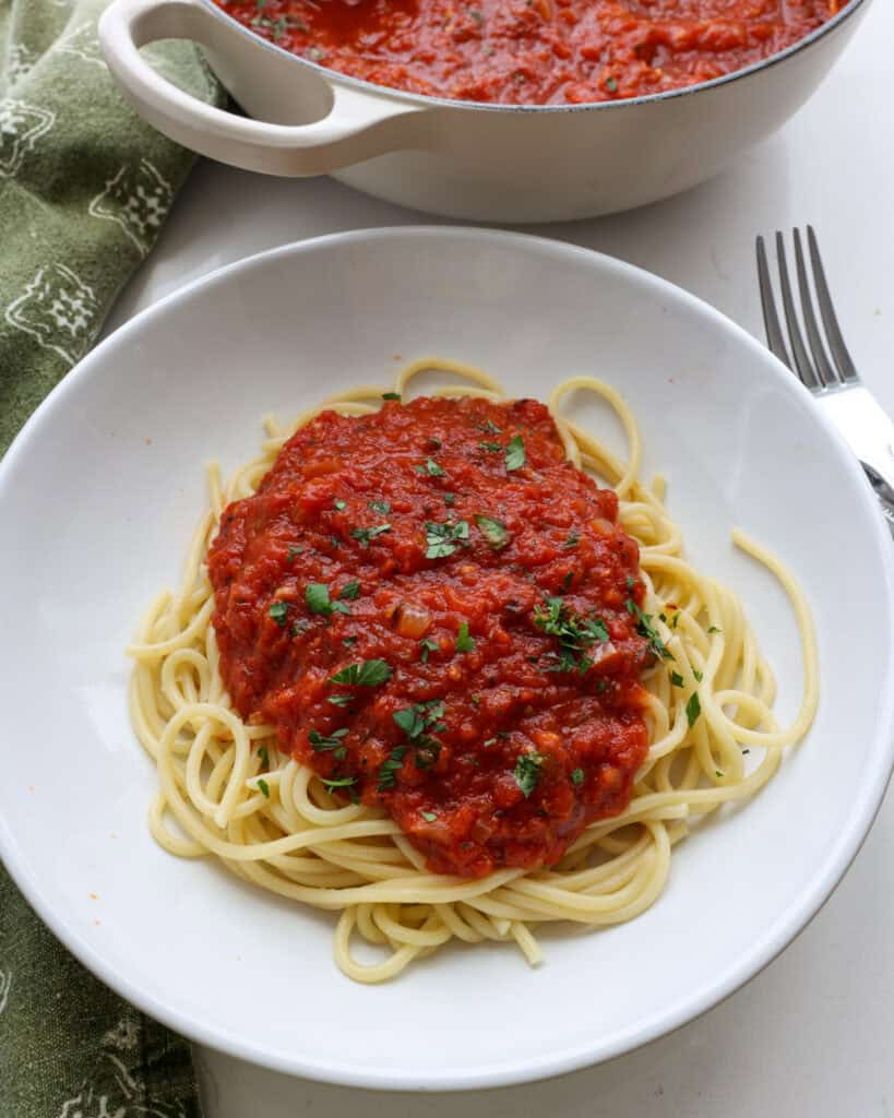 A bowl of spagheti covered with marinara sauce and chopped fresh parsley.