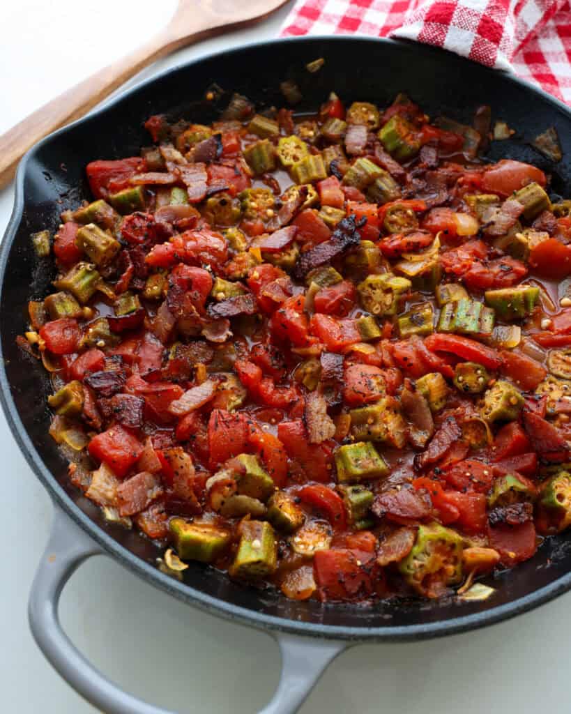 A skillet full okra and tomatotes with bacon, garlic, and onions.