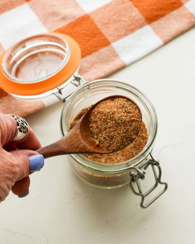 A wooden spoon full of pork chop seasoning over a jar full of it. 