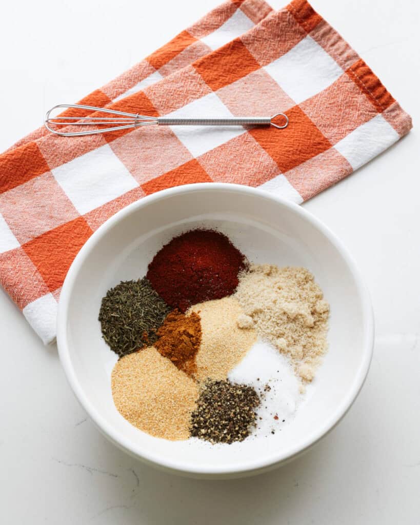 All the spice and herbs for pork chop seasoning in a wide bowl with a whisk in the background. 