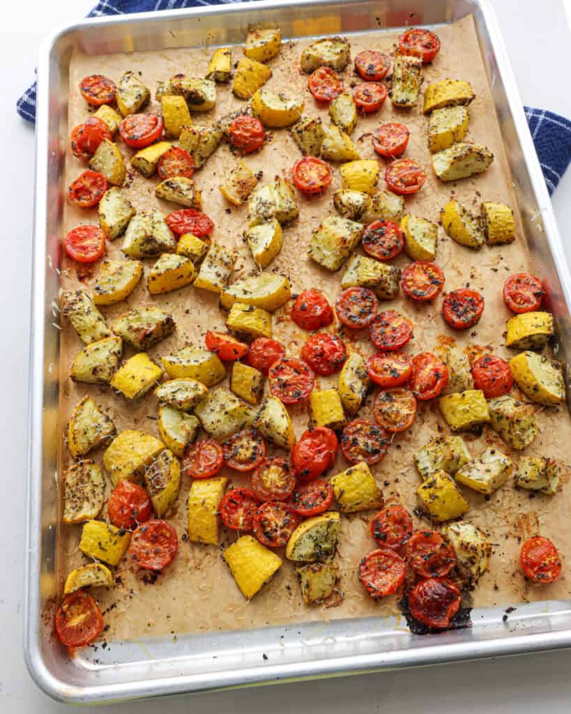 Roasted yellow squash and roasted tomatoes on a baking sheet covered with parchment paper.