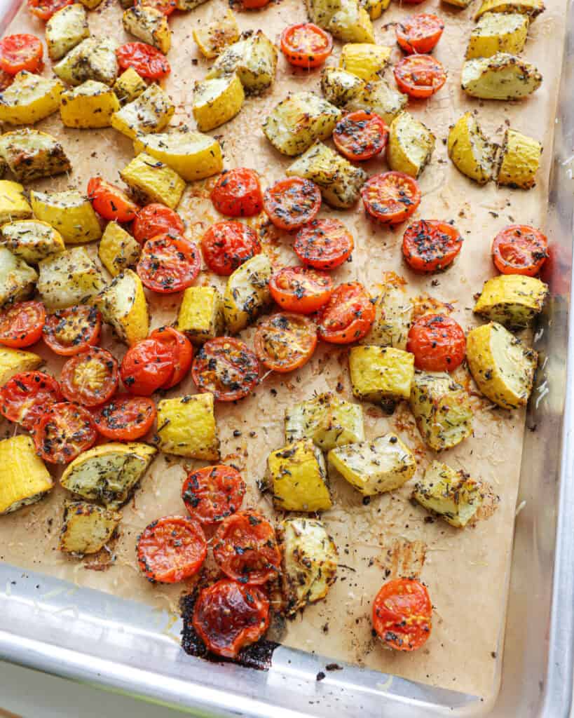 A large baking sheet with roasted yellow squash and roasted toimatoes.