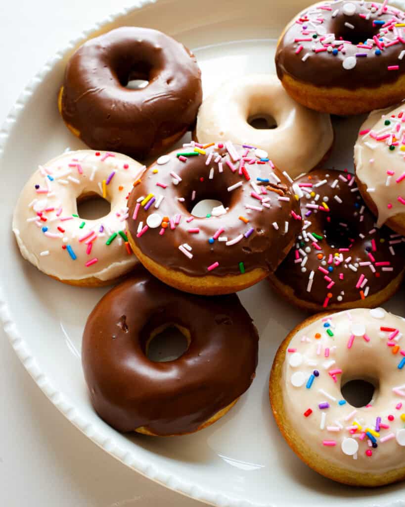A close up view of baked donuts with chocolate and vanilla glaze on a round white platter.
