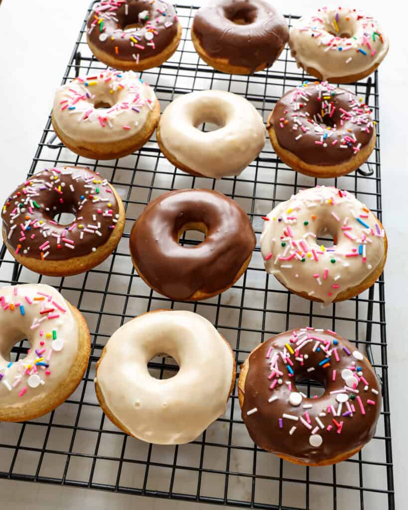A dozen donuts with assorted glaze on a cooling wire rack.