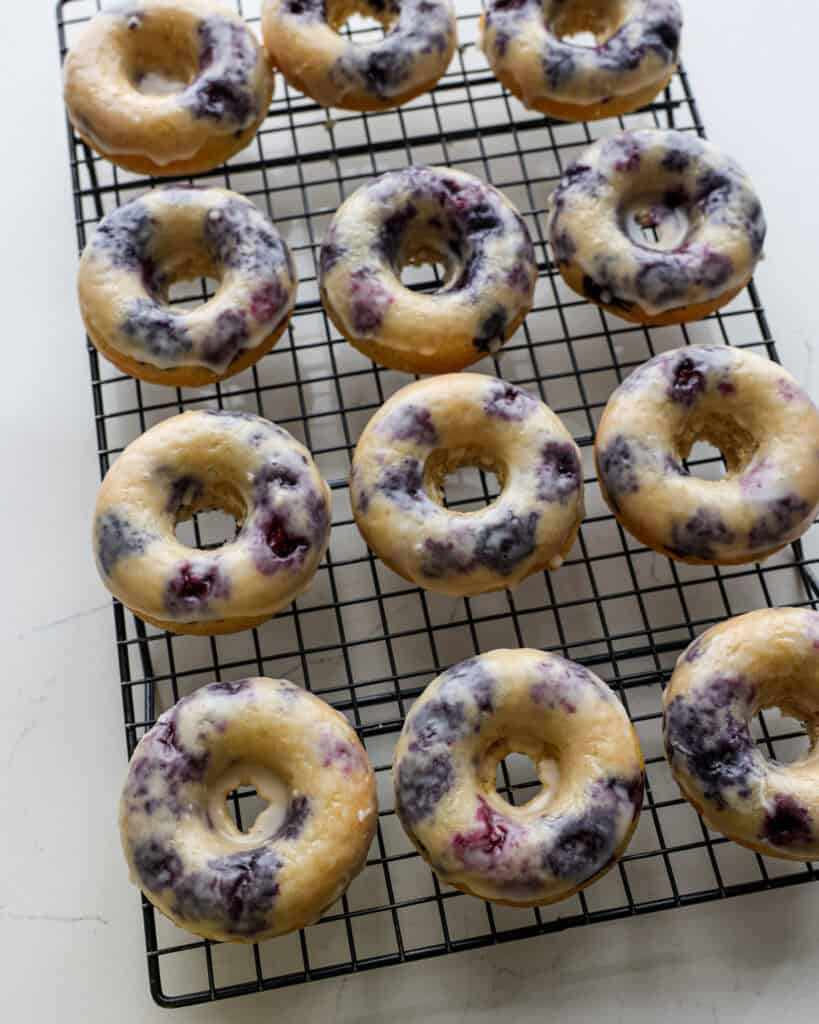 A dozen blueberry cake donuts cooling on a wire rack.
