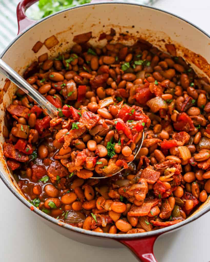 A close up view of a ladle and Dutch oven full of borracho beans.