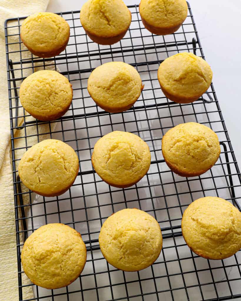 An overhead view of a dozen cornbread muffins on a cooling rack.