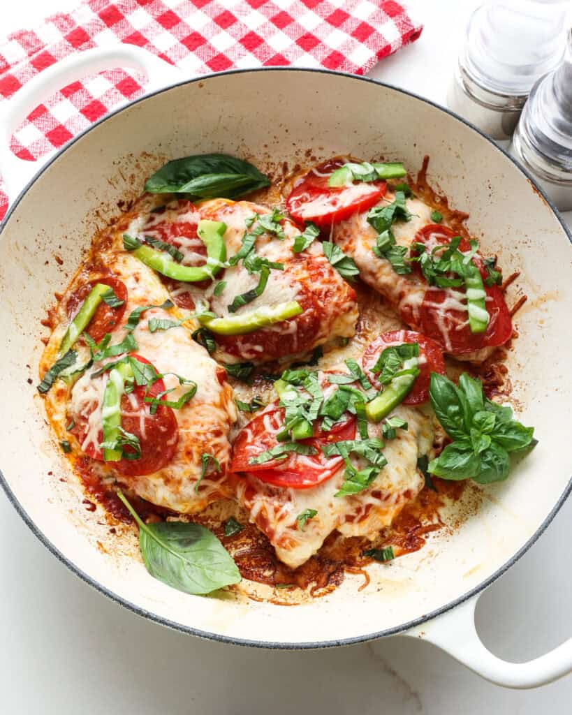 An overhead view of pizza chicken in a lare=ge white skillet.