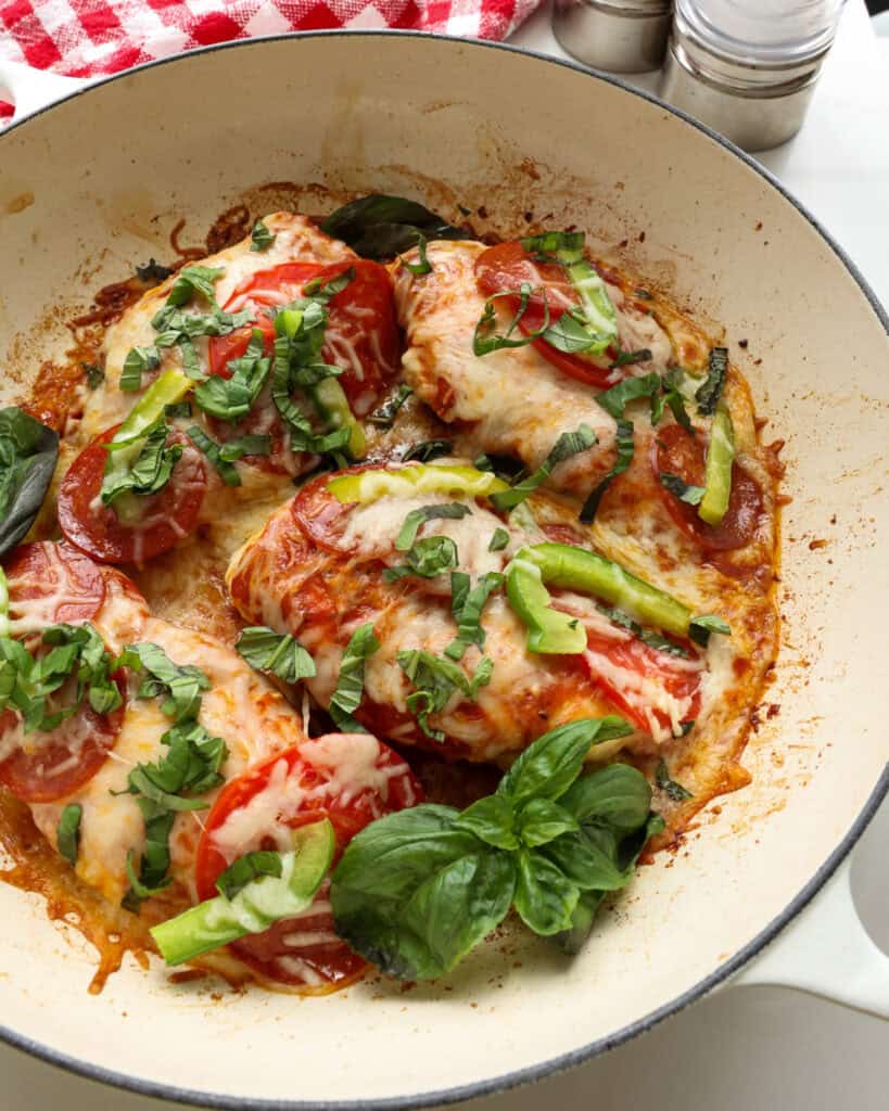 Pizza chicken with pepperoni and green bell peppers in a large white skillet.
