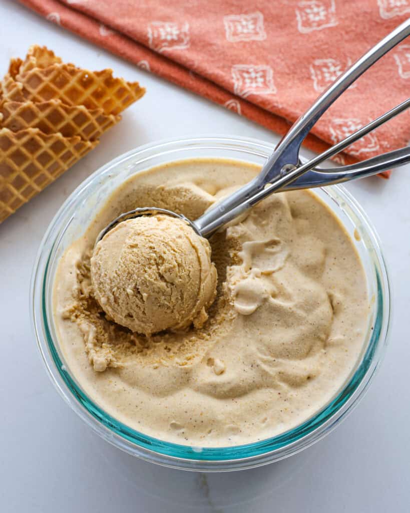 A ice cream scoop and glass bowl full of pumpkin ice cream. 