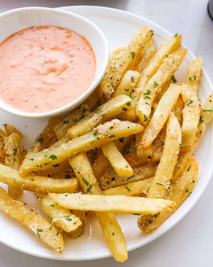 A close up view of truffle french fries and a small bowl of comback sauce on a serving plate. 