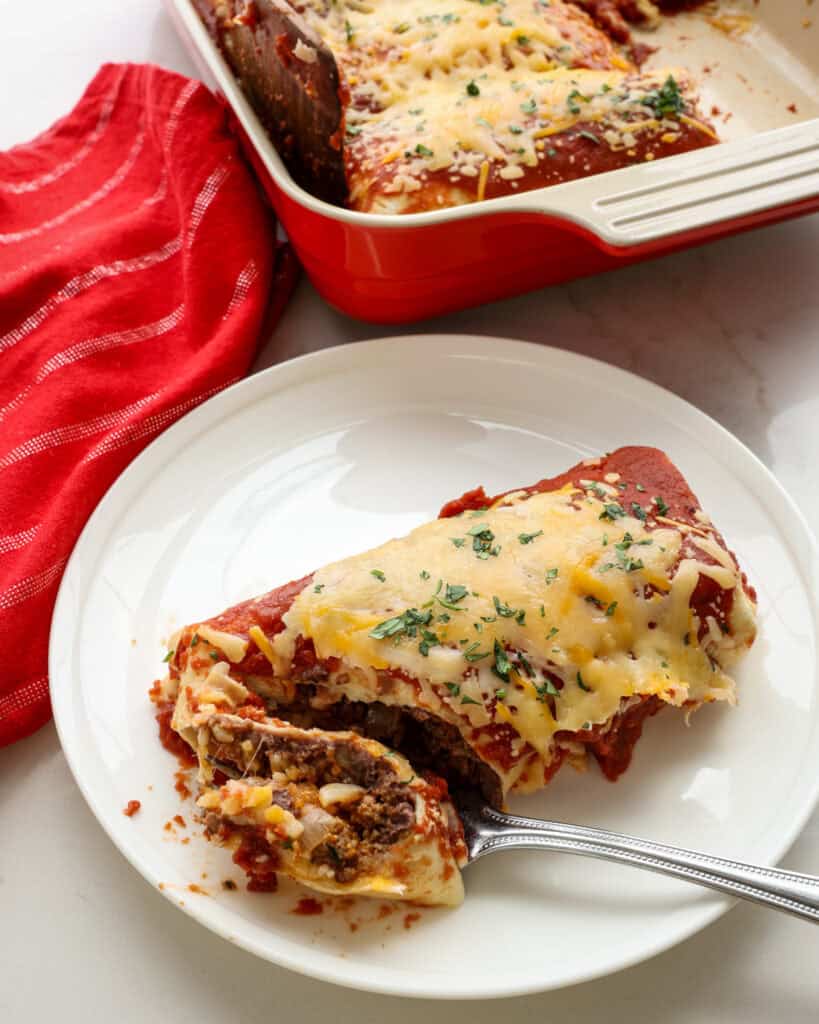 A wet burrito on a single serving plate with a bite on a fork. The rest of the casserole is in the background.