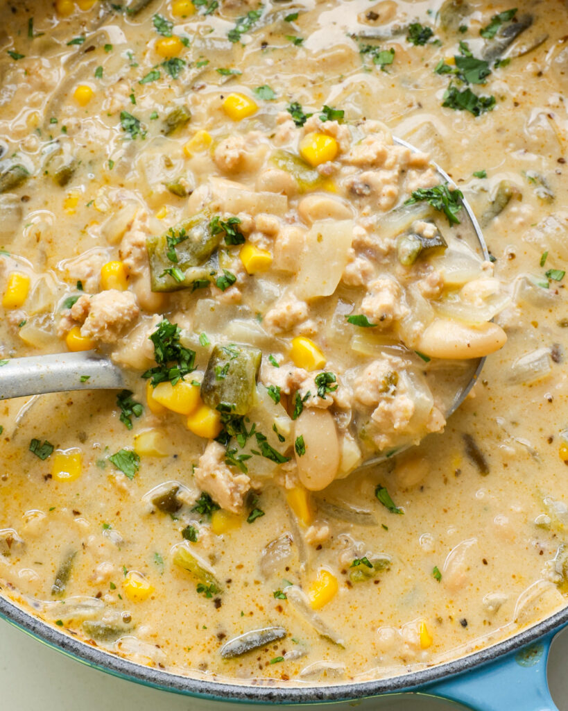 A close up view of a ladle full of white turkey chili. 