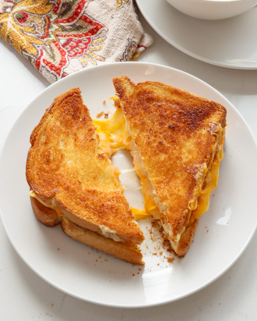 Air fryer grilled cheese on Texas toast on a white serving plate with soup and a napkin in the background.