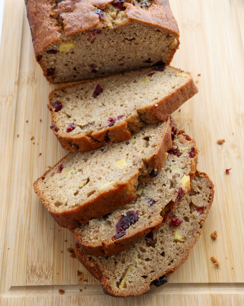An overhead view of a sliced loaf of appleasauce bread with apple chunks and cranberries.