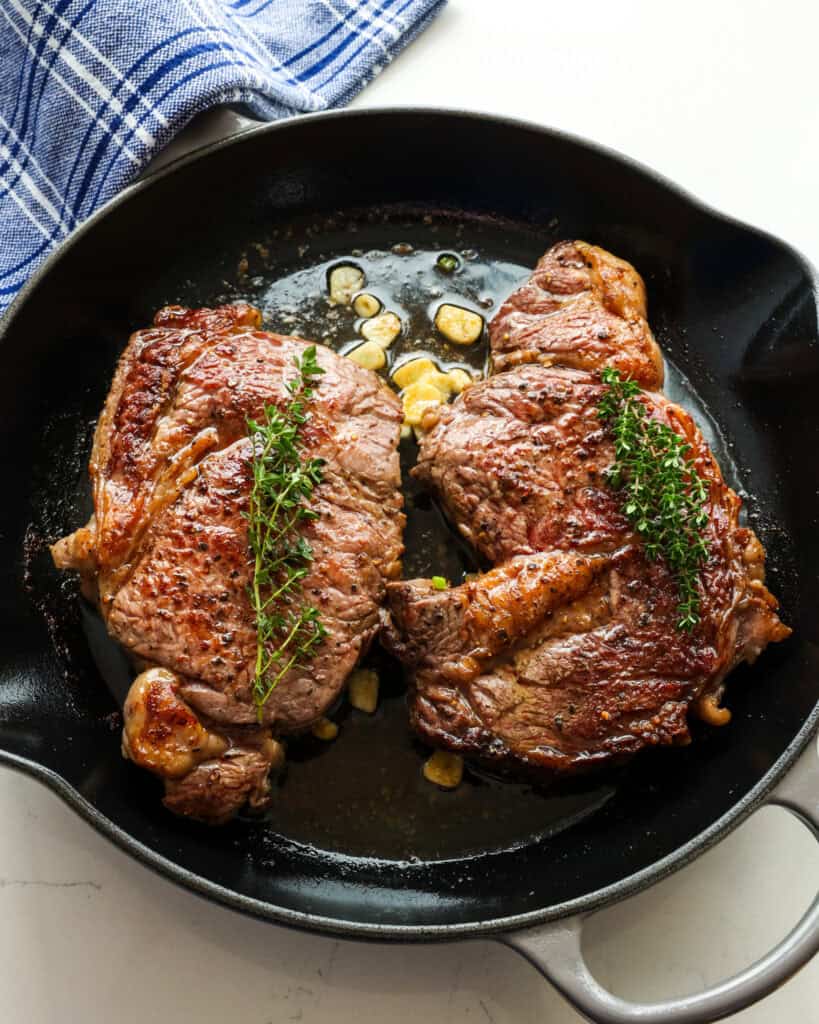 Overhead view of 2 ribeye steaks cooked in a cast iron skillet.