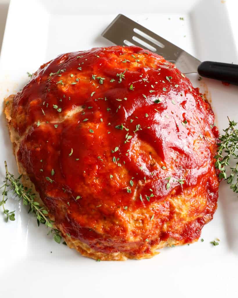 An overhead view of a whole chicken meatloaf on a large white serving platter.